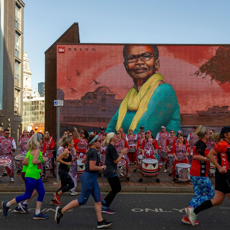 People running in front of a drumming band and colourful street art