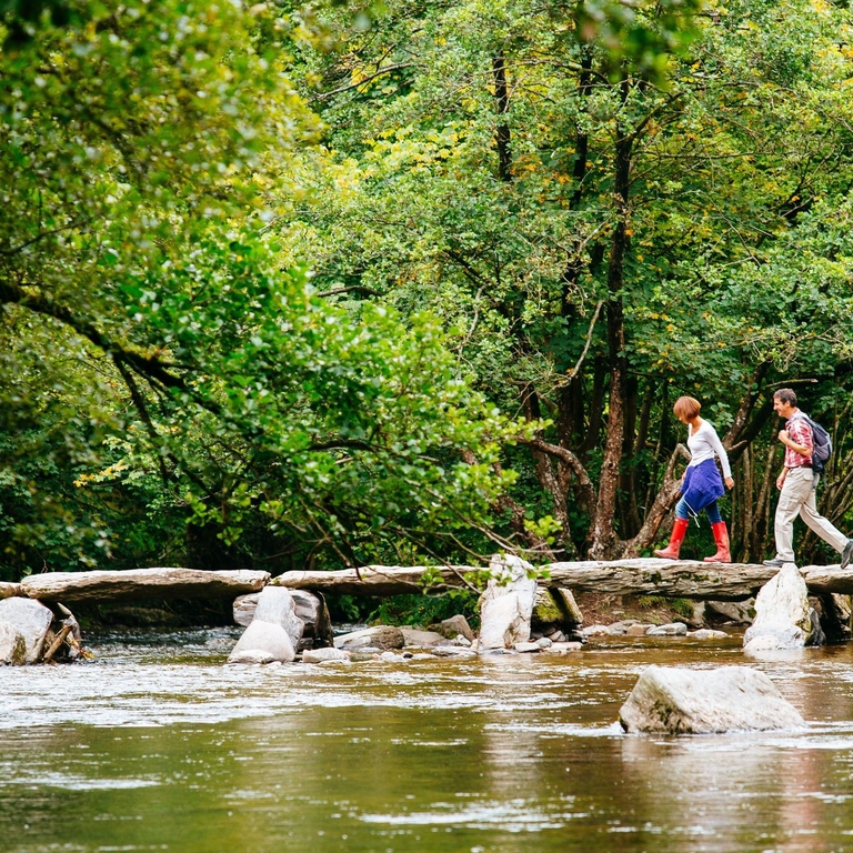 A man and woman walking over the river at clapper bridge