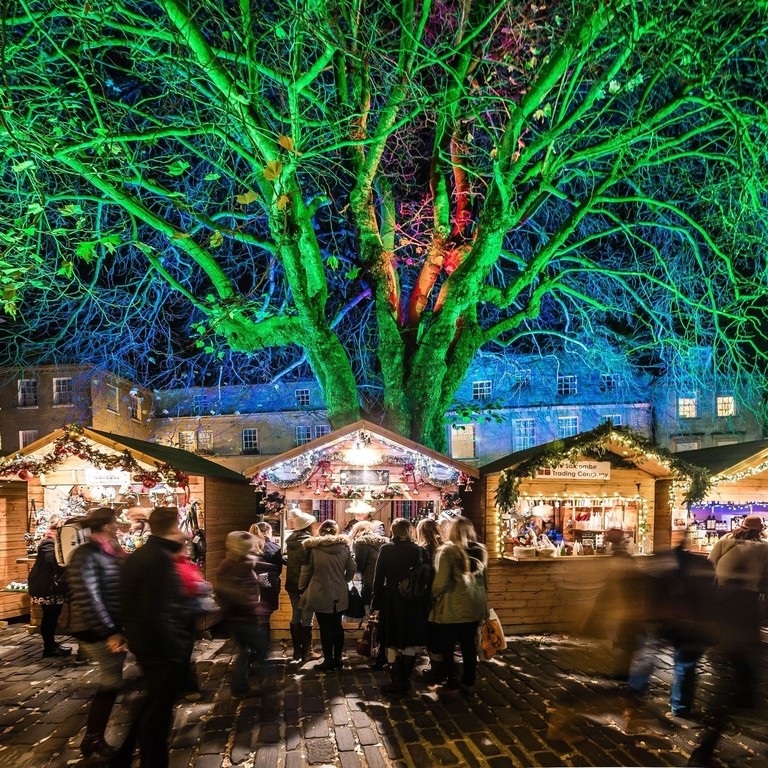 People visiting Christmas Market traders in wooden chalet huts in Bath