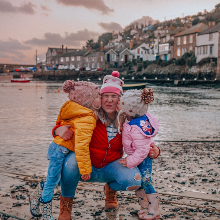 Two children giving a woman a kiss on the cheek on a beach