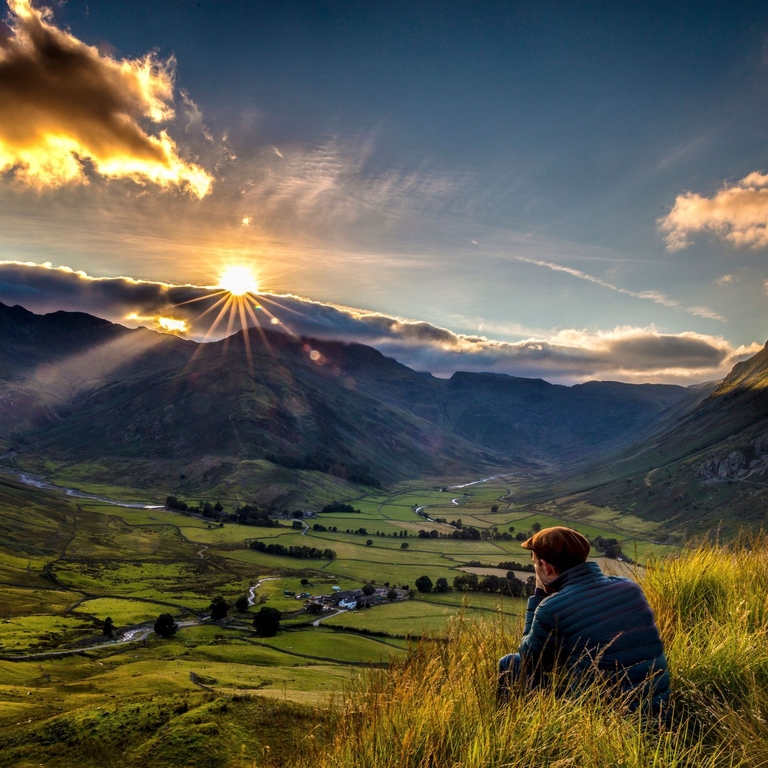 Man sitting in long grass watching sunrise between valleys