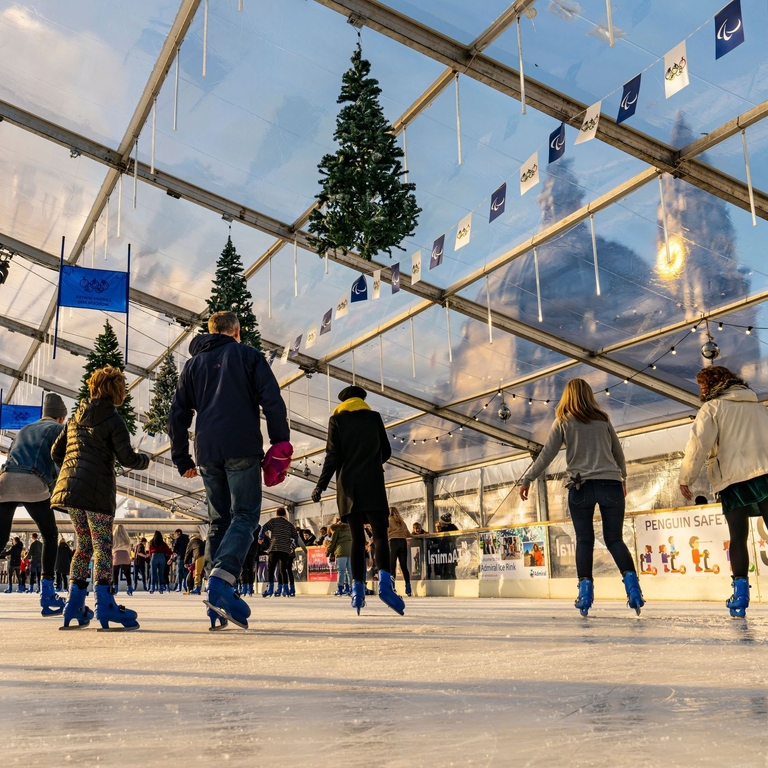 People ice skating on a skating rink under glass ceiling