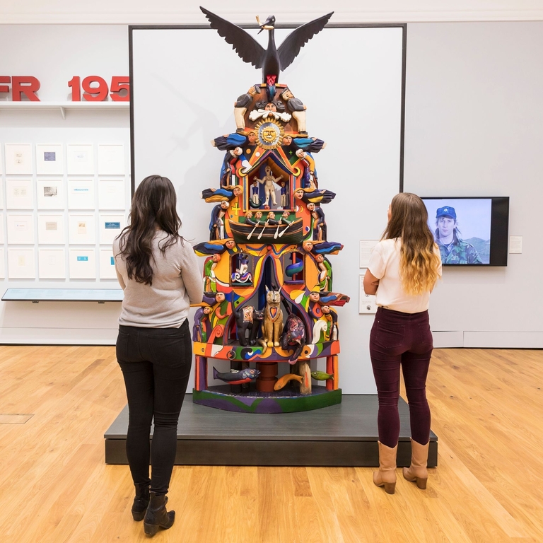 People admiring a sculpture of a totem pole in an art gallery. 