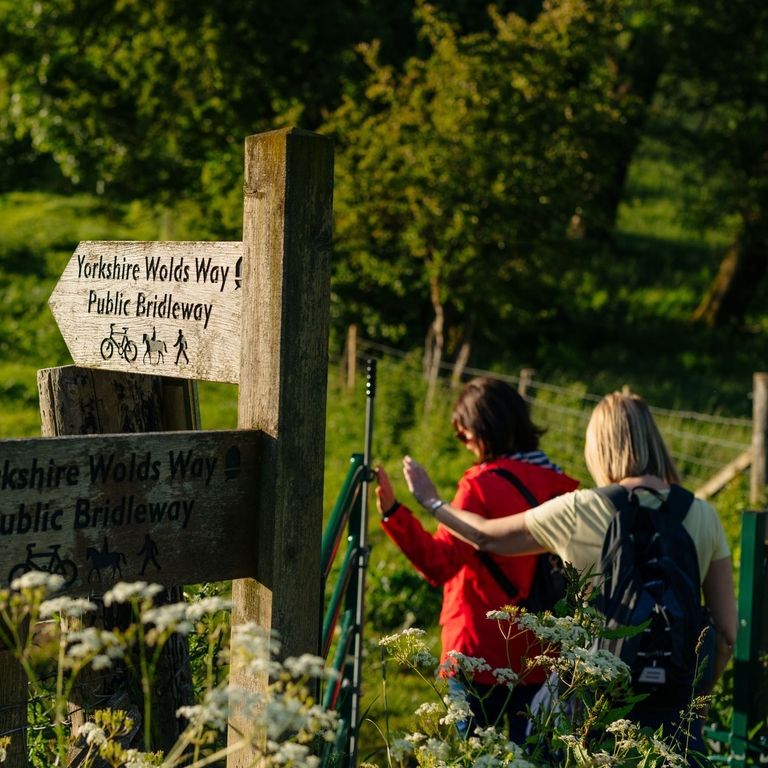 Two women walking in countryside passing sign posts