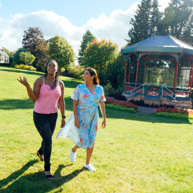 Two women walking on grass past a pergola