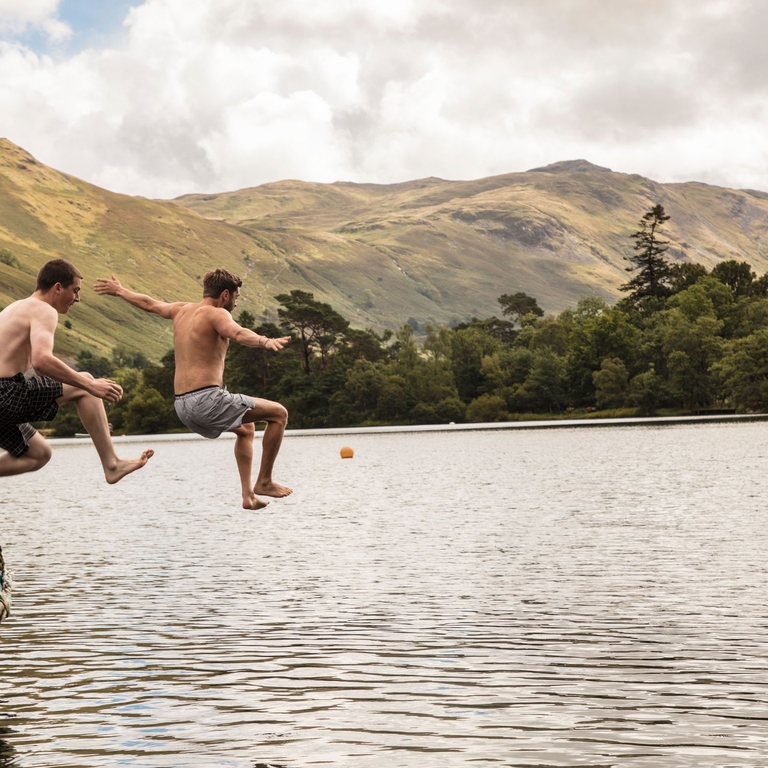 Two men in swimming shorts jumping off a boat into the lake