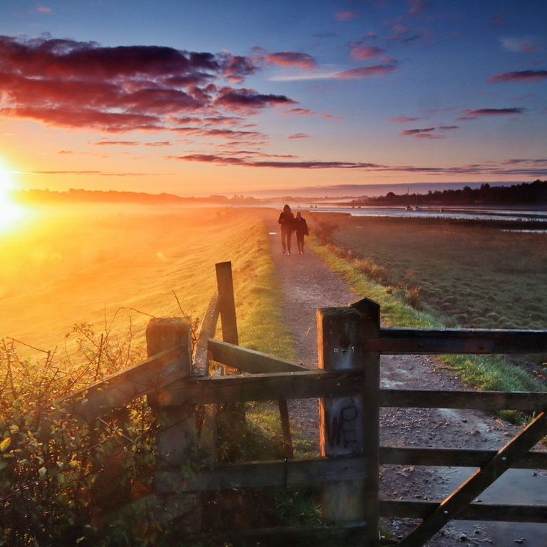 Two people walking along trail at sunset with gate in the foreground