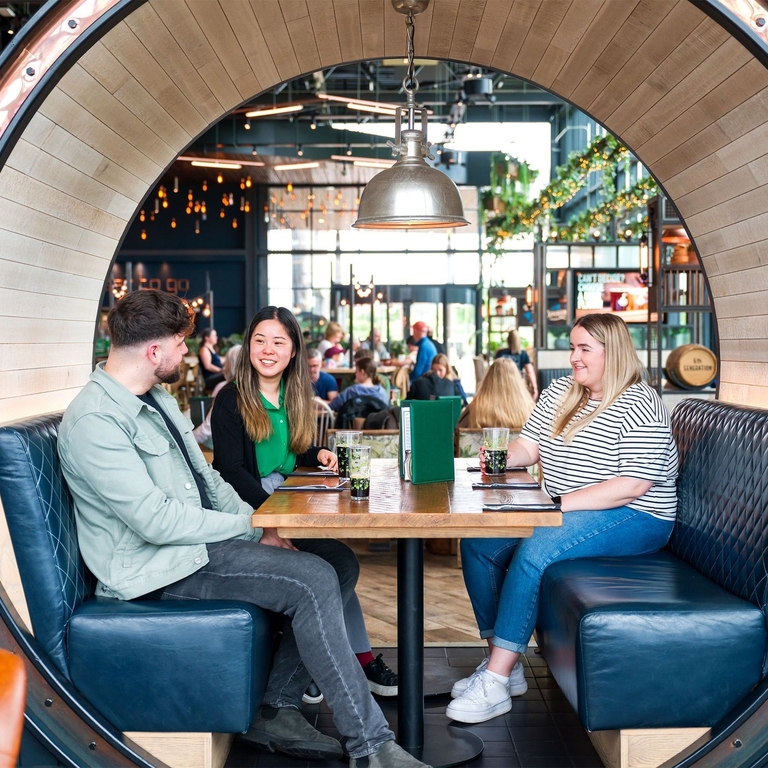 Two women and a man sit in a booth at a restaurant