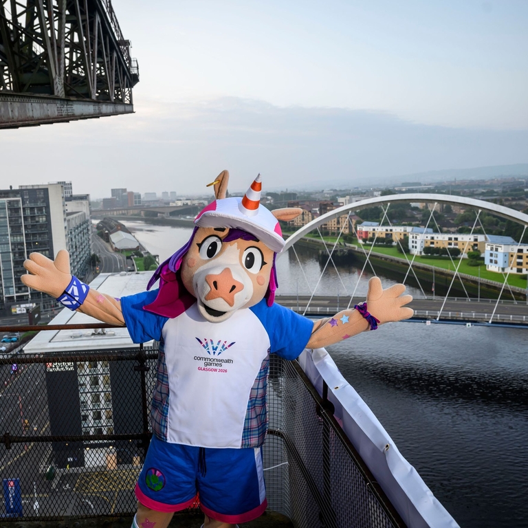 A games mascot posing on top of a balcony overlooking a river.