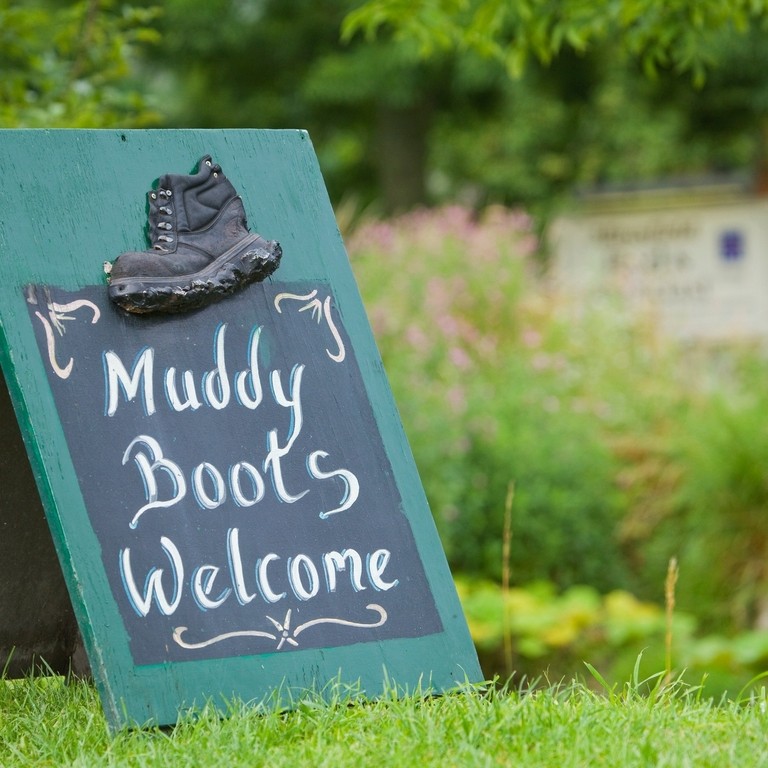 Signage on grass saying 'Muddy Boots Welcome' with plants