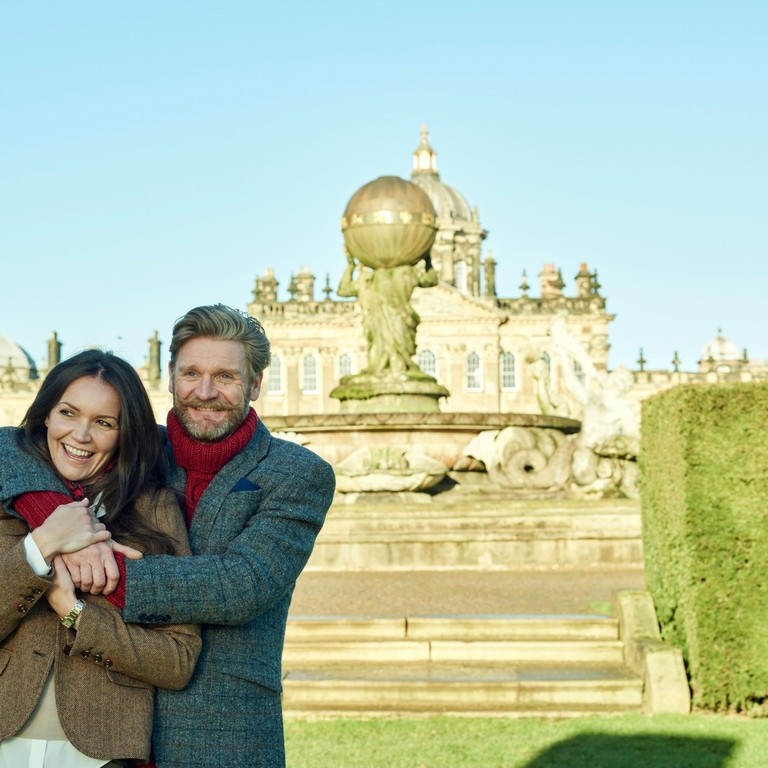 A man with arms wrapped around a woman in castle grounds