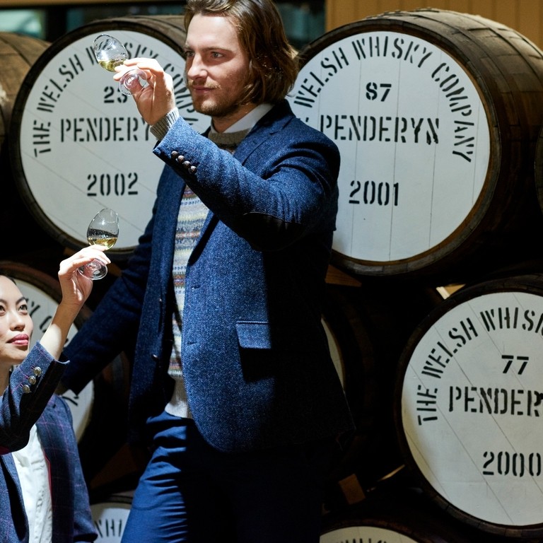 A man and a woman standing next to a stack of oak barrels