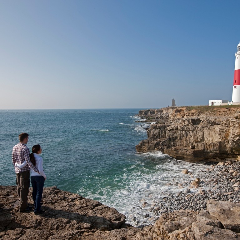 Couple looking at red and white lighthouse over coastline