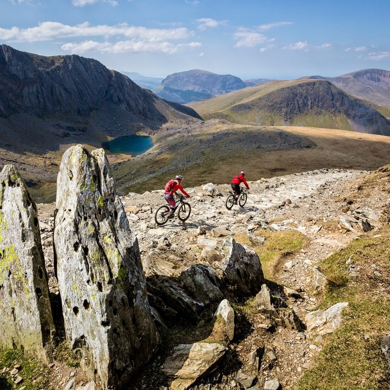 Two mountain bikers riding on the stoney path. Lake ahead