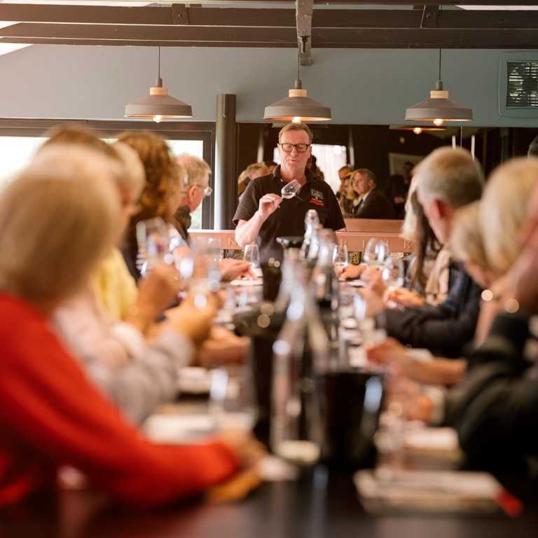 Large group of people sitting at long table at wine tasting