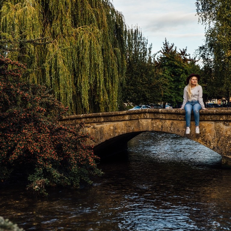 Blond woman wearing hat and jeans sitting on bridge