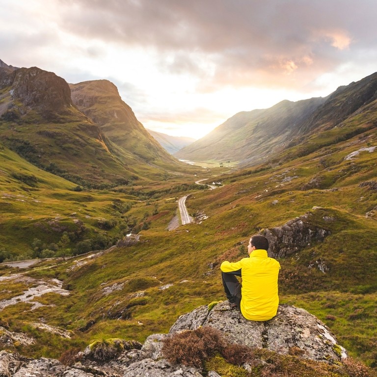 Man in yellow jacket sat on a rock looking out at valley