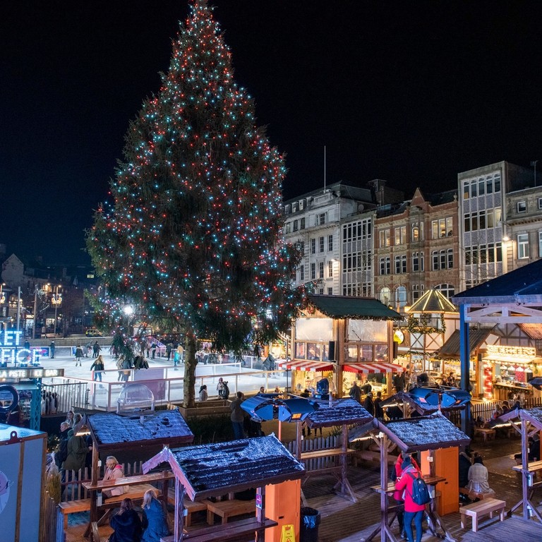 People around wooden chalets and a lit-up helter skelter in the background at Nottingham Christmas Market