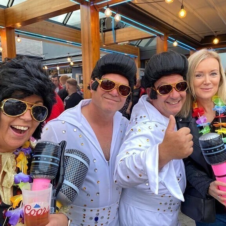 Two Elvis impersonators posing with people at the Elvis Festival in Porthcawl, Wales