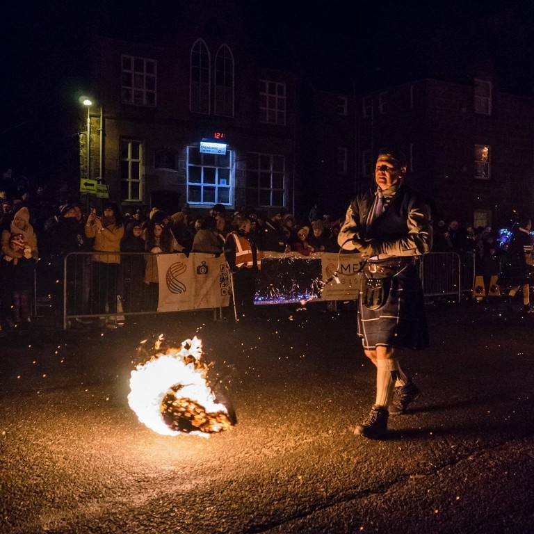 A man whirling a fireball on a stick at a parade in Stonehaven