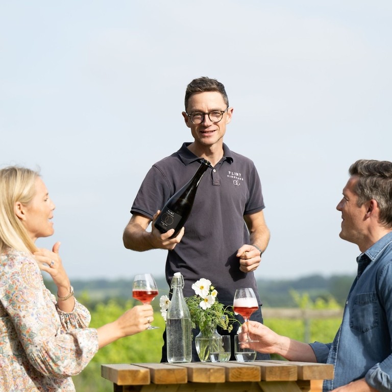 A waitor serving wine to a couple in a vineyard