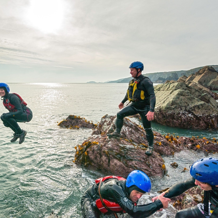 People coasteering off rocks into the ocean.