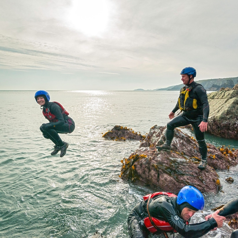 People coasteering off rocks into the ocean.