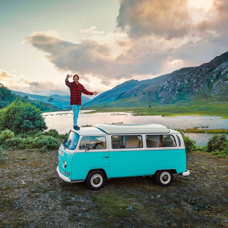 Man standing on camper van taking a selfie on the shore 
