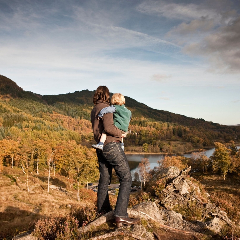 Woman and child standing on a hilltop overlooking a lake.