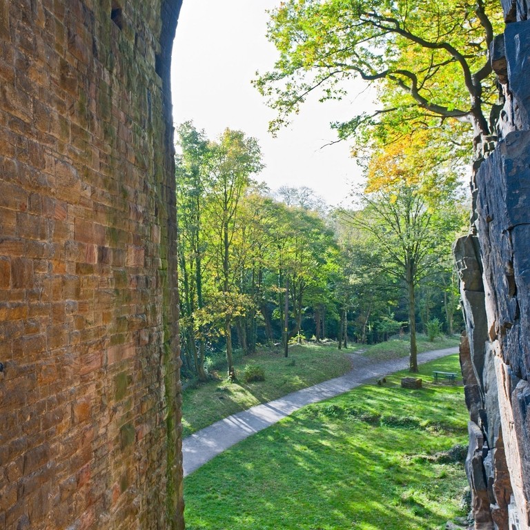A climber using climbing gear scaling the underside of the arch of a bridge