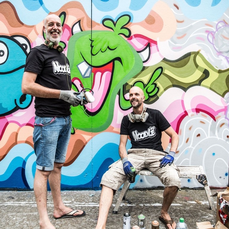 Artistas callejeros con botes de pintura cerca de coloridas obras de arte