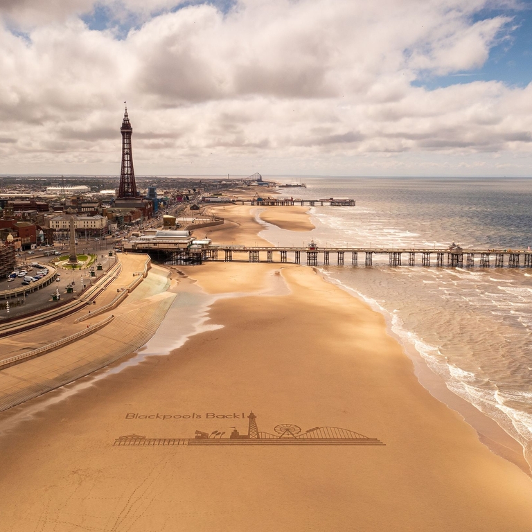 Landscape shot of a sandy beach with a pier and tower.