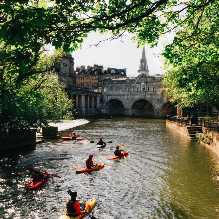 Group of people kayaking on the river in the sunshine by Pulteney Bridge, Bath