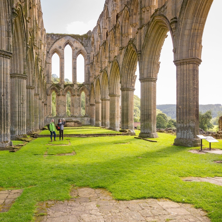 Two people explore the ruins of Rievaulx Abbey.