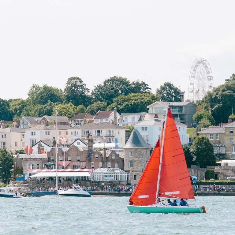 Red sailing boat sailing in front of a coastal town