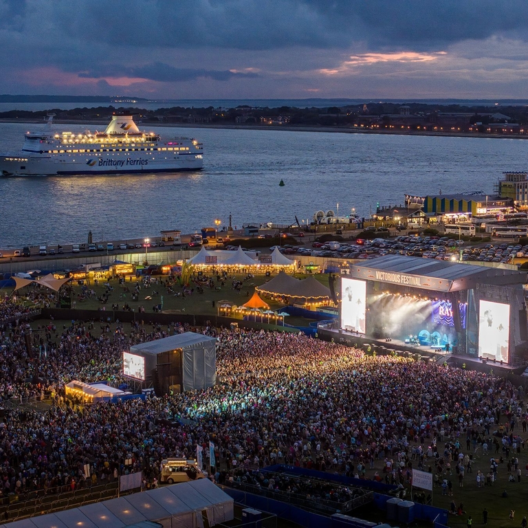 Aerial shot showing crowds at a music festival next to the ocean