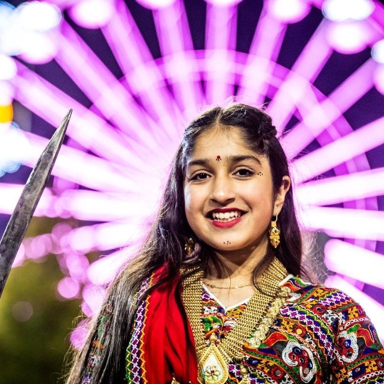 A woman celebrating Divali in front of a large lit up wheel