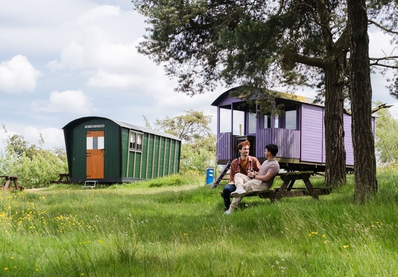 Two men sat oustide a shepherds hut in the countryside