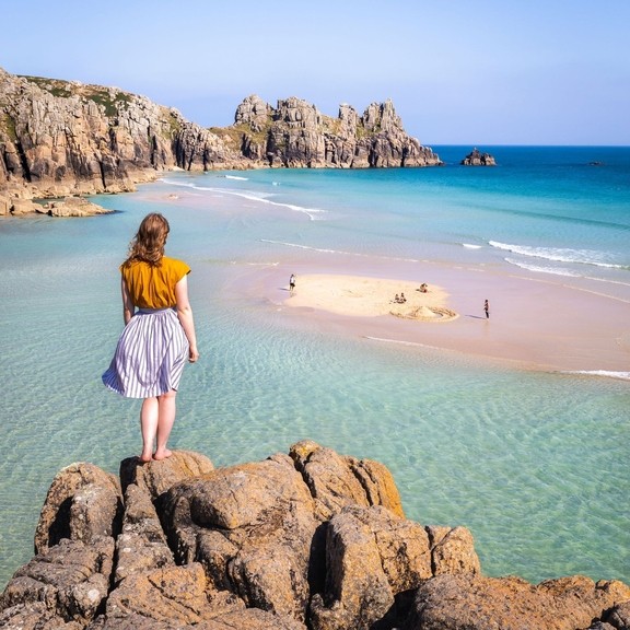 Frau, die auf einem Felsen steht und auf das Meer hinausschaut