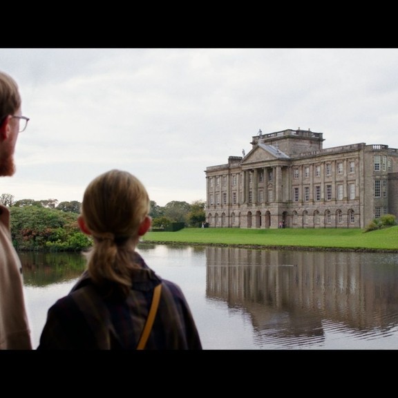 A man and a woman stand across a lake looking toward a heritage house