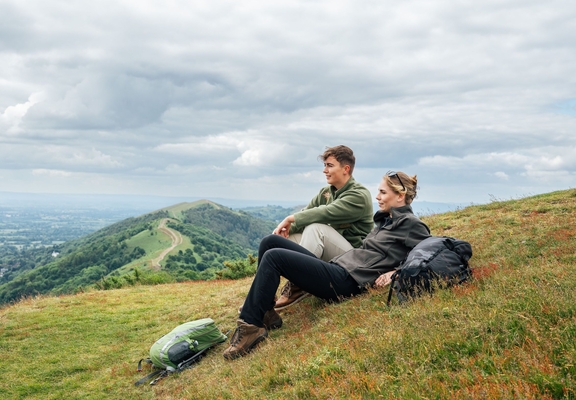 Two women sit on a hill looking toward a view with green hills beyond