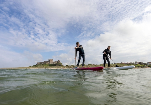 Two men on are paddleboarding in the sea with a heritage castle in the background.