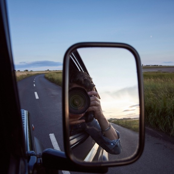 Reflection of man with camera in side view mirror of car