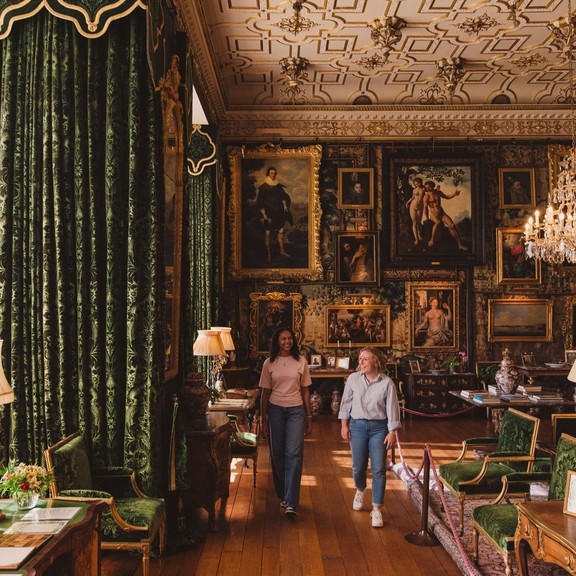 Two women walk through an ornate room in a heritage house