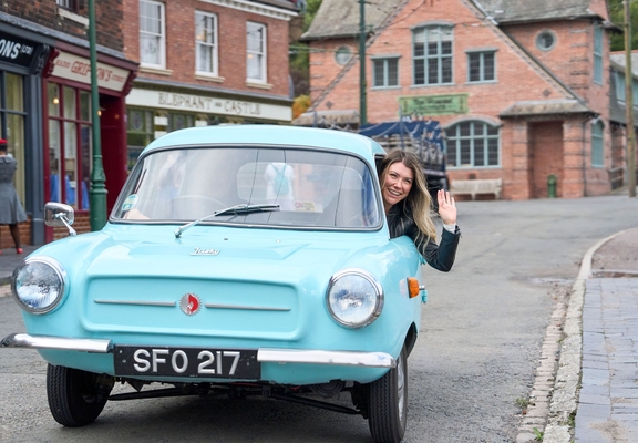 A woman waving and smiling inside a vintage car at a living museum