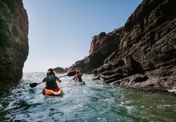 A man and a woman sea kayaking along a rocky outcrop.