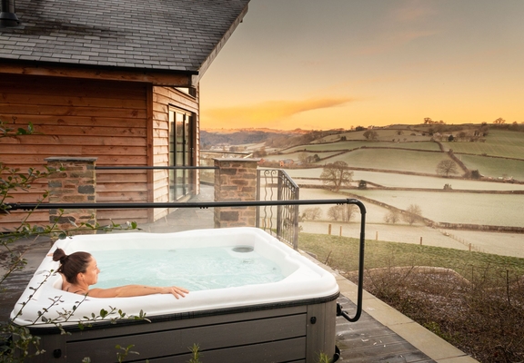 A woman in an outdoor Hot Tub,looking out across rolling farmland in the morning mist.