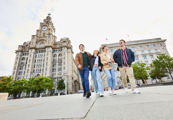 Four friends exploring a local city walking along waterfront promenade, with historic buildings in the background