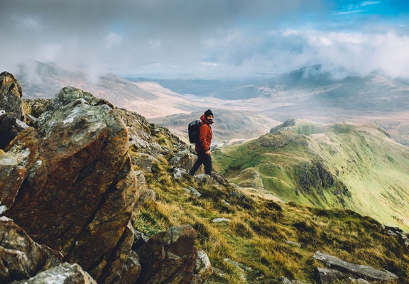 A rugged up man navigating the panoramic summit of a large mountain range 