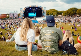 People sitting down and watching the stage at a music festival